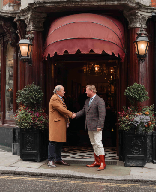 two men in suits shake hands outside of pub in London